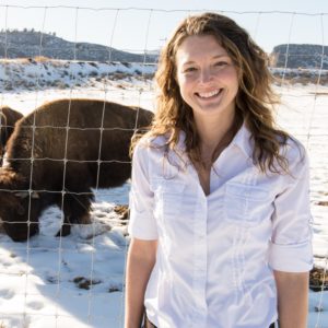 Jennifer Barfield standing in the snow in front of a fence with two bison behind it