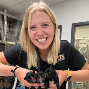 blonde woman smiling while holding three black puppies