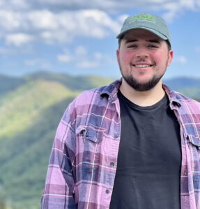 man wearing a baseball cap standing in front of a mountain