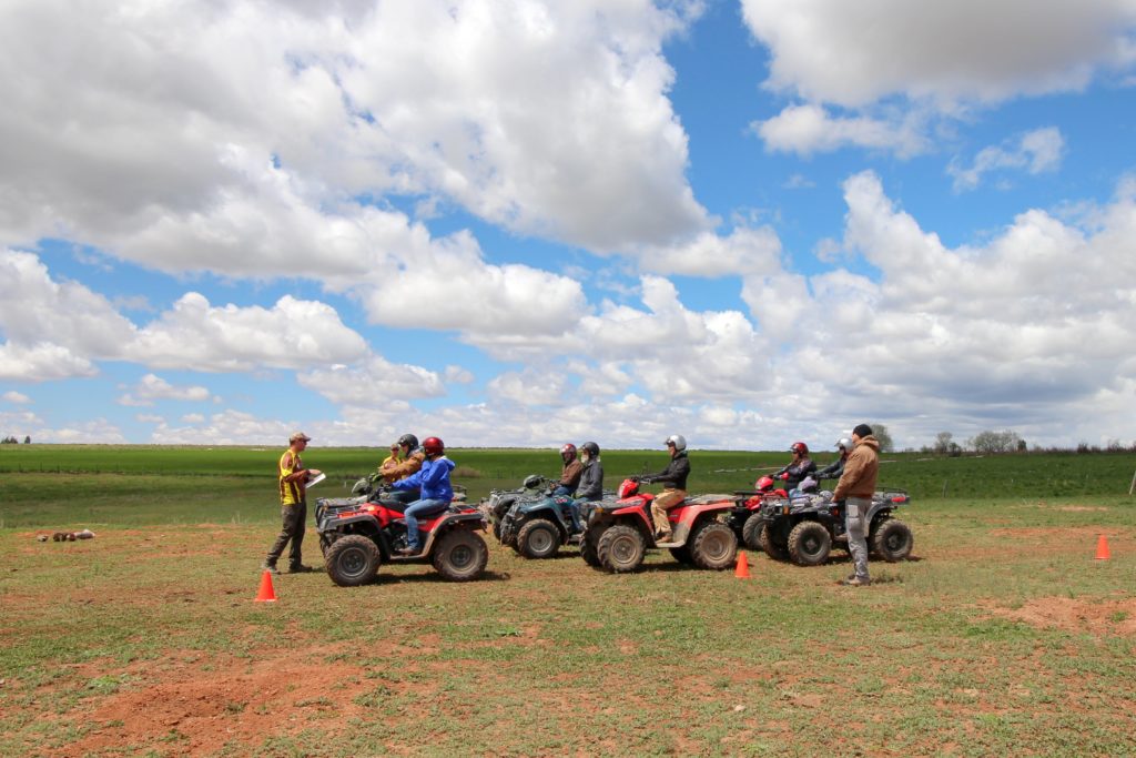 A man instructing six people on parked ATVs in a field