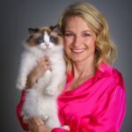 blond woman wearing a bright pink shirt holding a brown and white cat