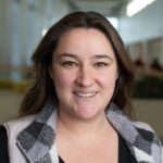 a person smiles at the camera with brown hair wearing a black and white checkered vest
