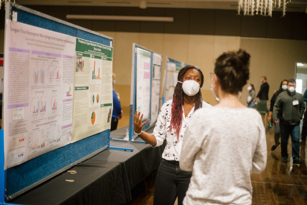 woman gesturing toward her research poster at Research Day