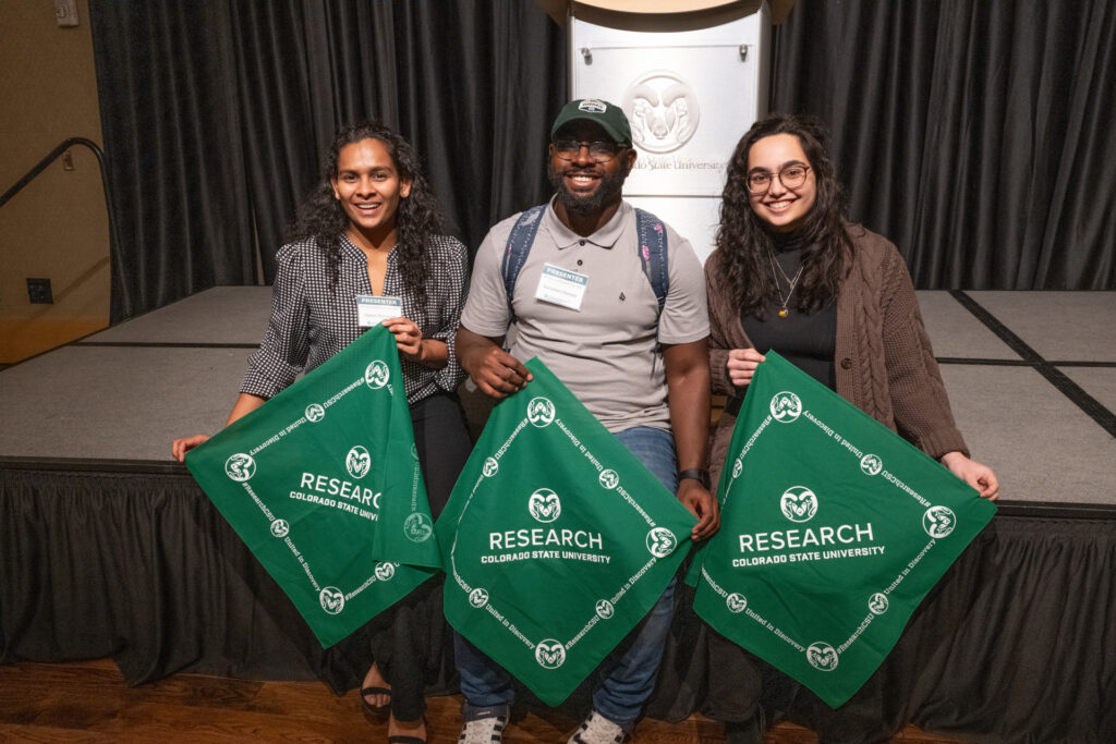 three students hold up green CSU research bandanas while smiling