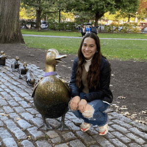 brown-haired woman squatting next to a bronze sculpture of a duck