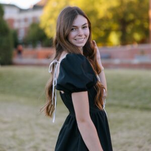 brown-haired woman wearing black dress, smiling in the grass