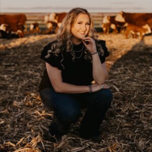 woman wearing black shirt and jeans squatting in a dairy field, smiling