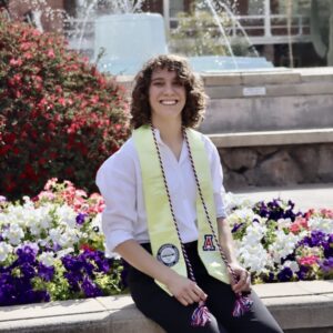 curly-haired person sitting on a bench next to flowers