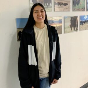 black-haired woman smiles standing in front of a wall