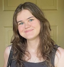 A person with brown hair smiles at the camera with a beige door in the background