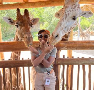 a person smiles at the camera, feeding the giraffes