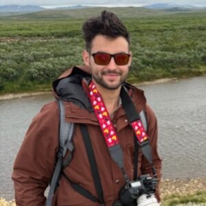 man smiling wearing a brown jacket and holding a camera